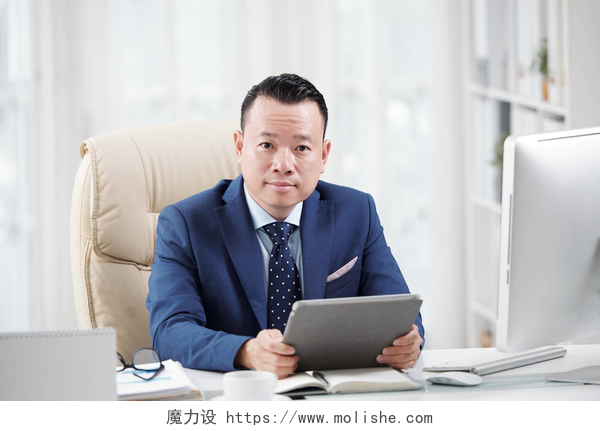坐在办公桌上办公的商务男士自信的越南企业高管与数字平板电脑在他的桌子上工作
